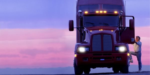 A silhouette of a truck driver getting into the cab of his commercial Class 8 truck tractor at